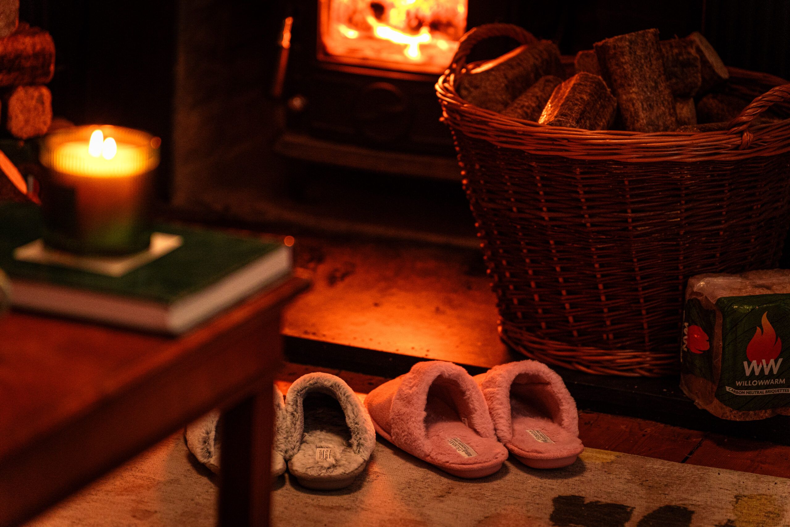 Two pairs of warm slippers on a rug in front of a WillowWarm fire