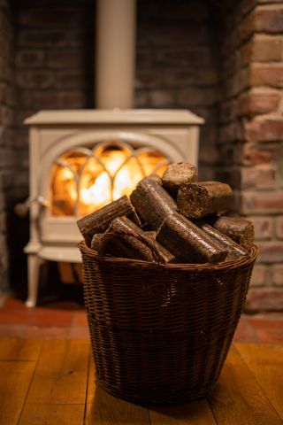 Briquettes sitting in a basket on a varnished floor with a lit stove in the background