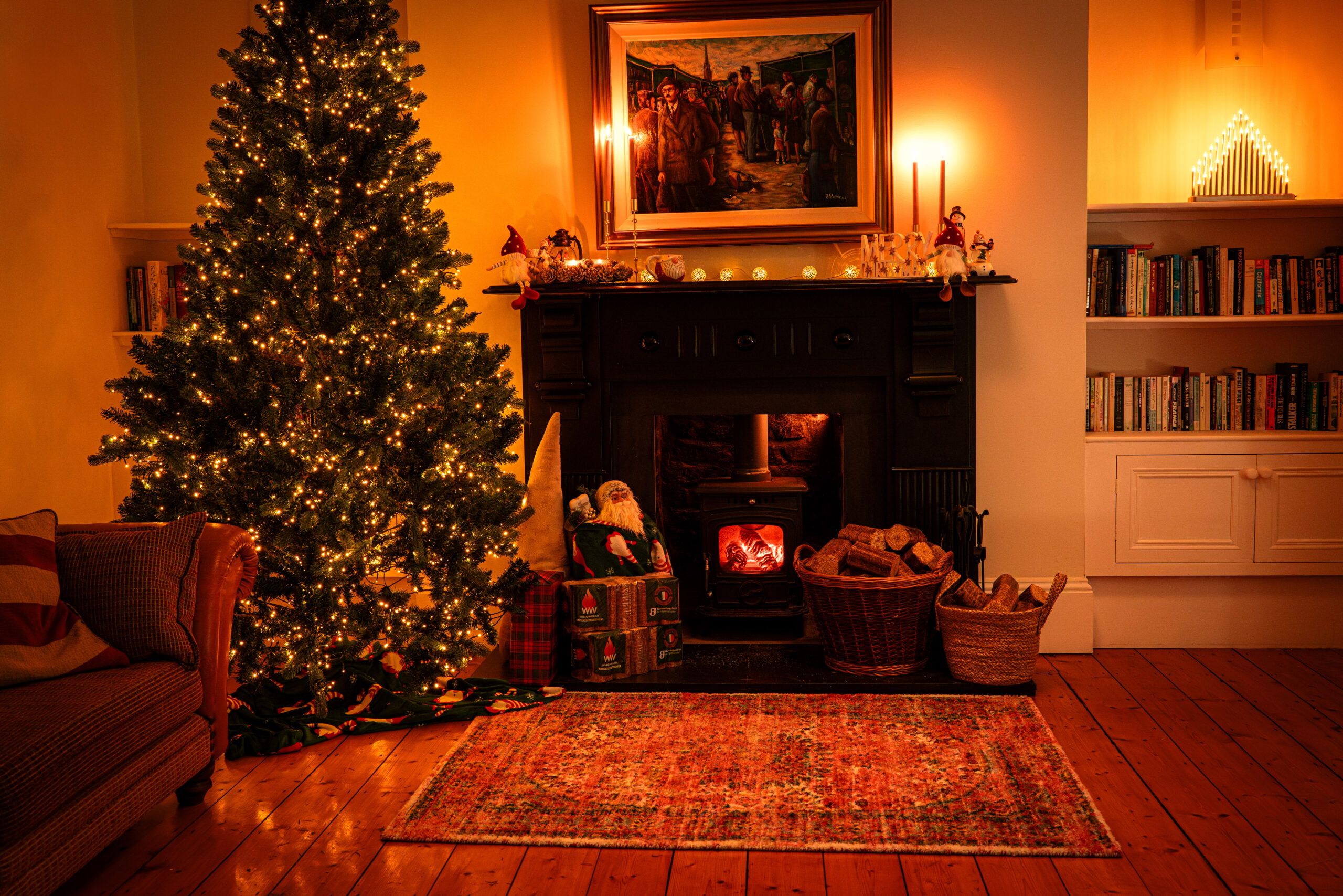 A Christmas tree in a room near a fireplace with WillowWarm fire and a basket of briquettes