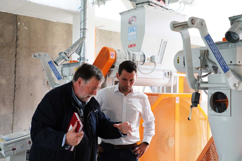 Two men standing together looking at manufacturing equipment
