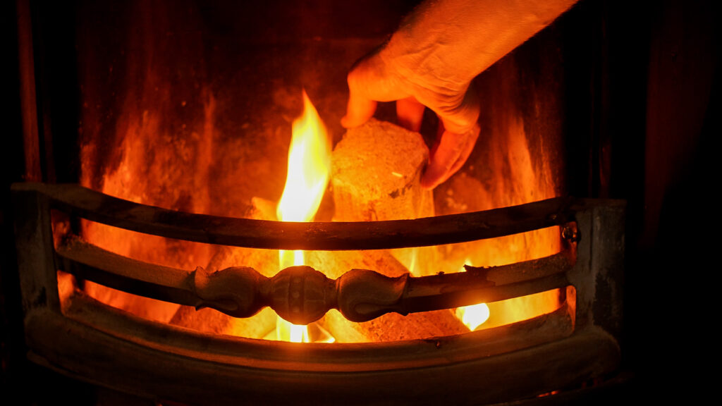 Hand putting a WillowWarm Briquette on an open fire