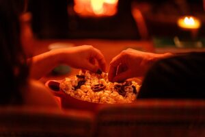 Hands reaching into a bowl of popcorn with a fire in the background