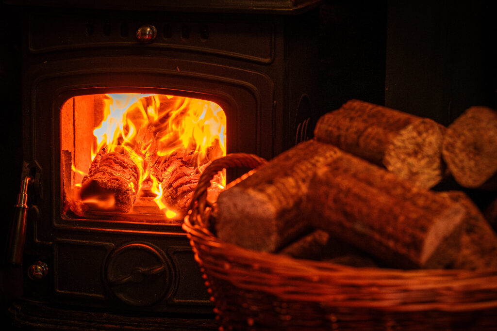 Basket with WillowWarm briquettes in front of a stove with WillowWarm