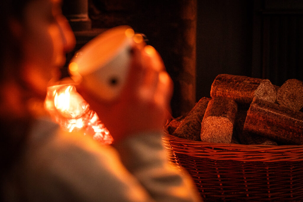 Woman holding a mug of soup to her mouth with a WillowWarm fire and briquettes in the background - one of 5 ways to keep warm this winter 