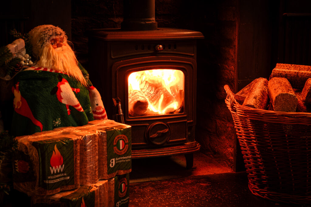 Santa sitting on WillowWarm bale with a WillowWarm fire burning to remind everyone to be safe with Christmas decorations