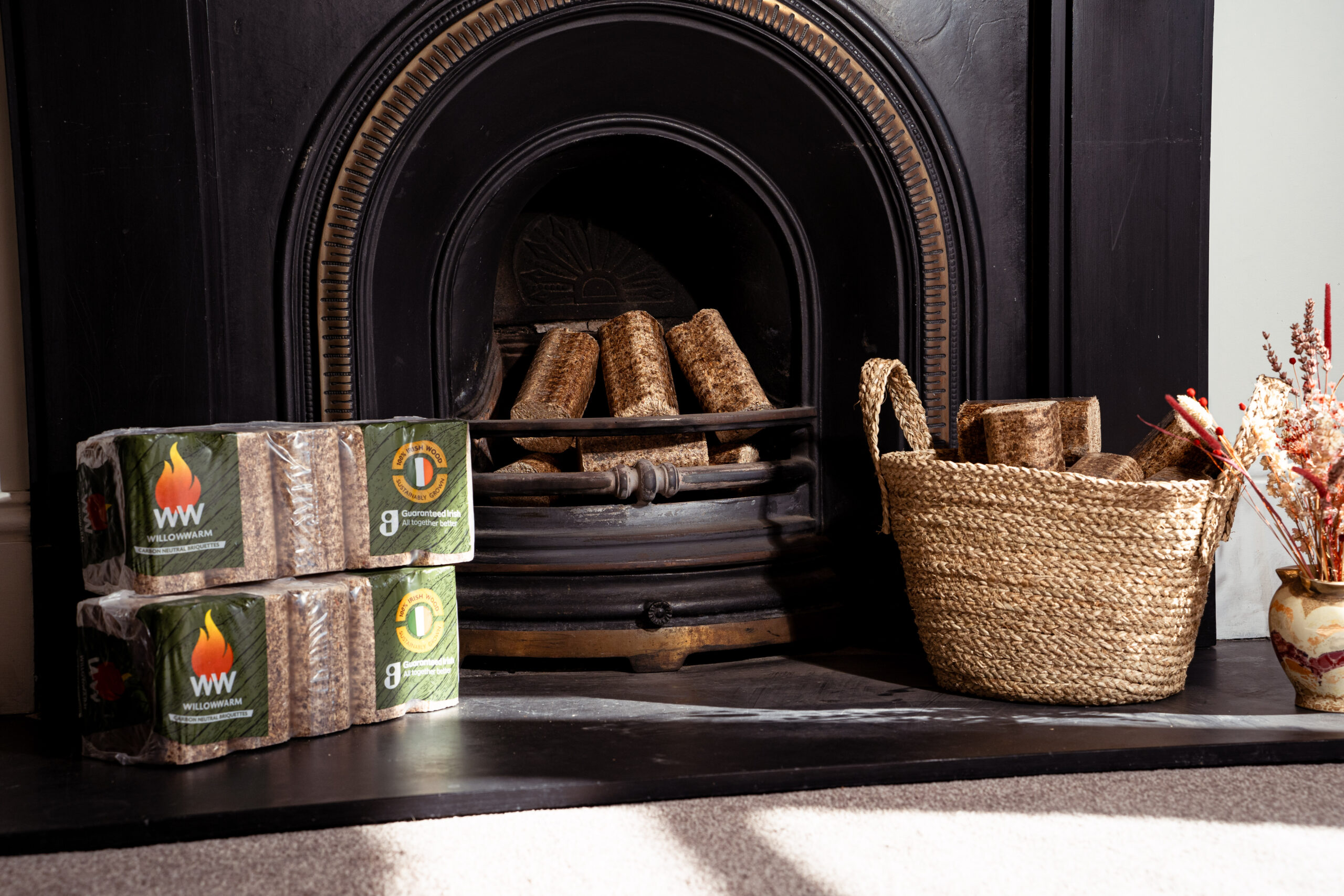An open fire with a basket of WillowWarm logs to the right and 2 bales to the left